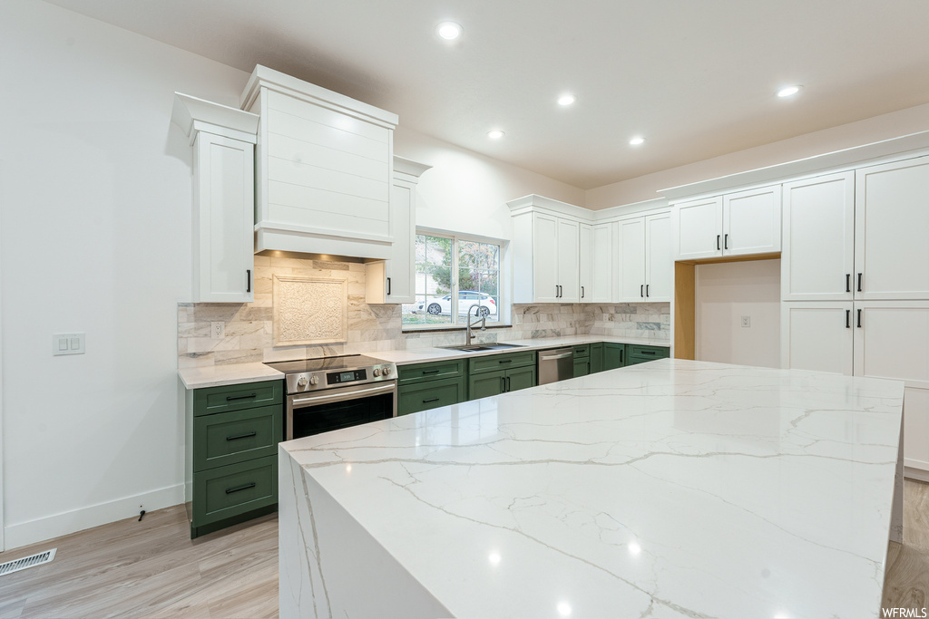 Kitchen with tasteful backsplash, sink, light stone countertops, white cabinetry, and stainless steel appliances