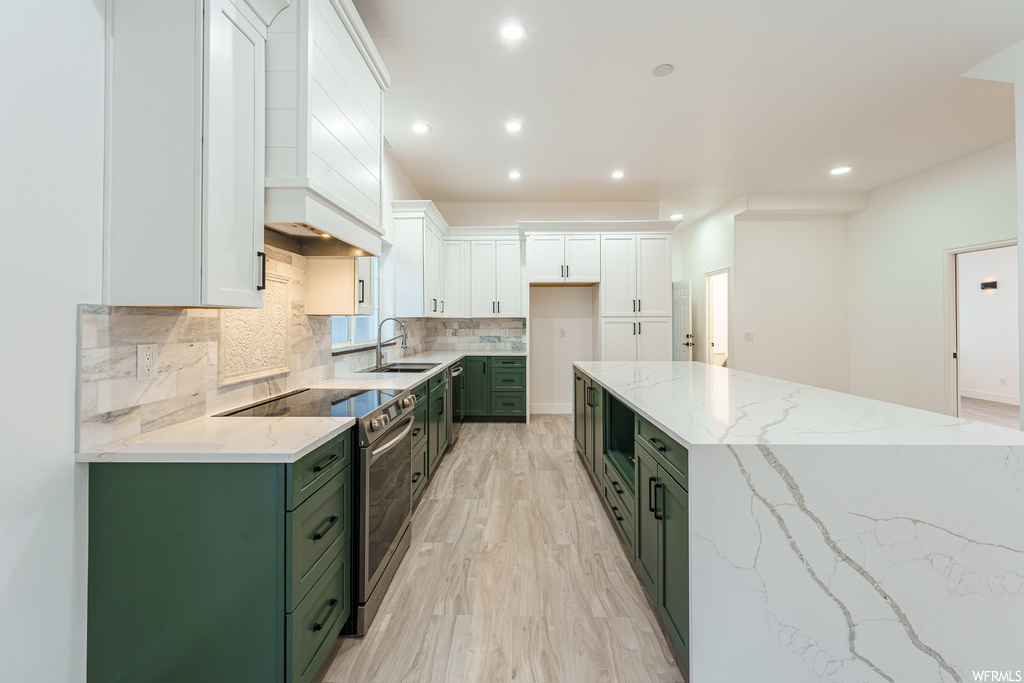 Kitchen with premium range hood, sink, light wood-type flooring, white cabinetry, and stainless steel electric stove