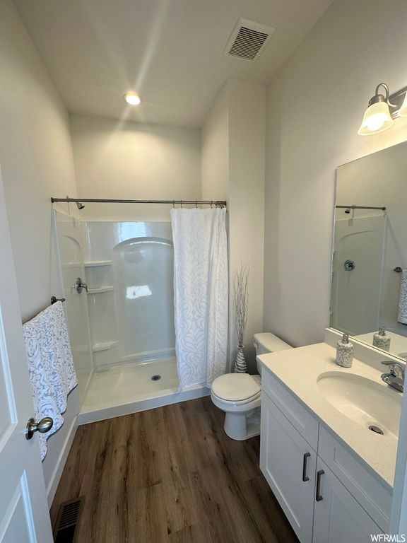 Bathroom featuring large vanity, wood-type flooring, curtained shower, and toilet