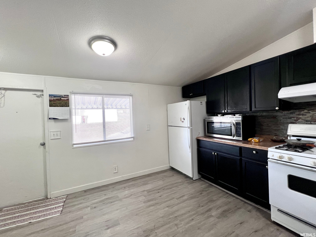 Kitchen featuring light hardwood / wood-style flooring, white appliances, lofted ceiling, and tasteful backsplash