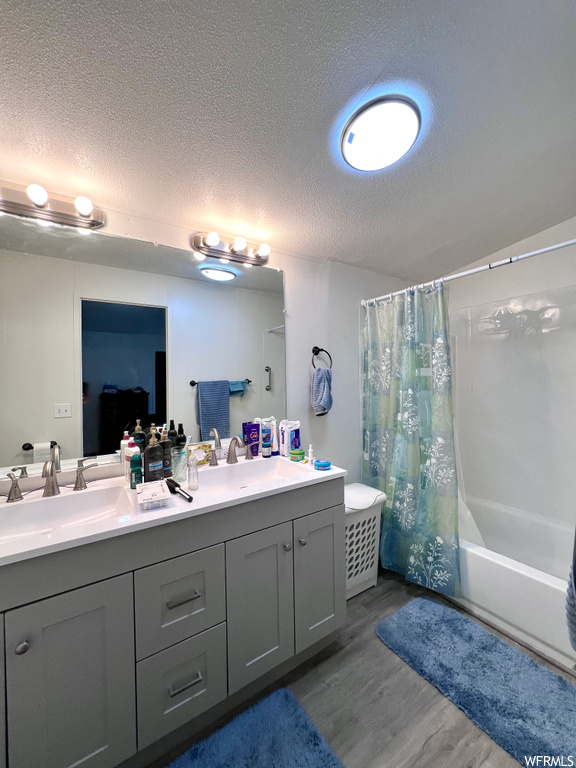 Bathroom featuring shower / bath combination with curtain, dual vanity, and a textured ceiling