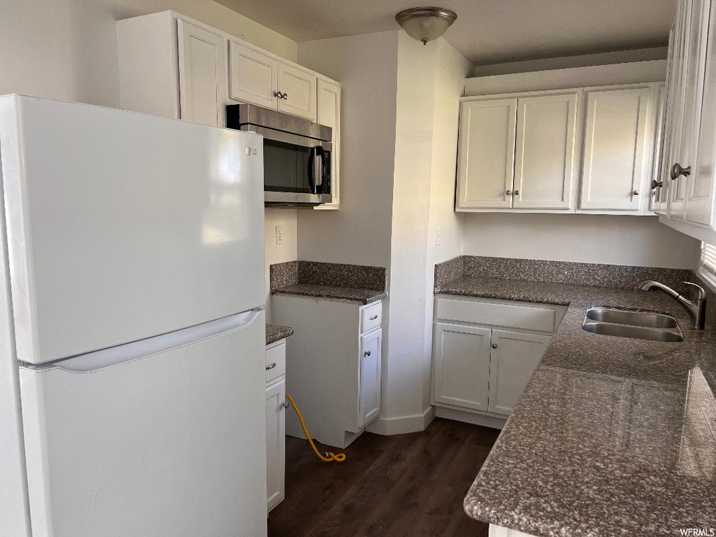Kitchen with dark hardwood / wood-style flooring, white refrigerator, sink, dark stone countertops, and white cabinetry