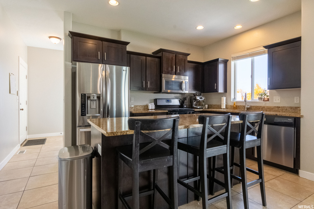 Kitchen with a kitchen island, dark stone countertops, dark brown cabinets, and stainless steel appliances
