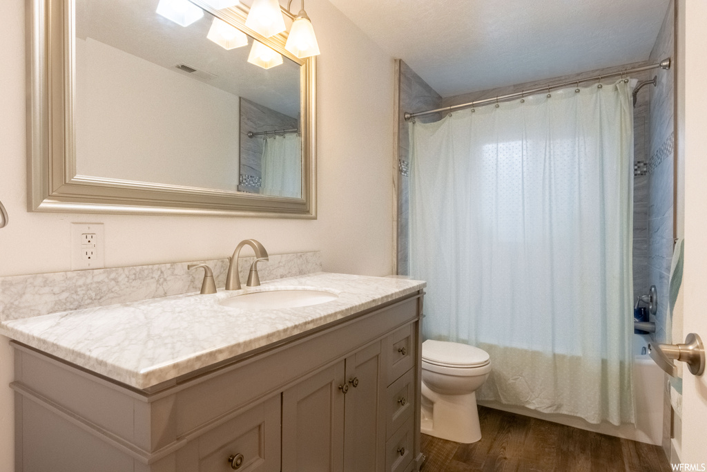 Full bathroom with toilet, hardwood / wood-style floors, shower / bath combination with curtain, and vanity with extensive cabinet space