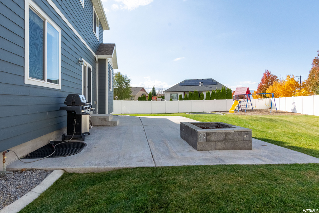View of patio with a playground, an outdoor fire pit, and a grill