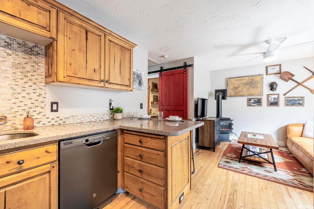 Kitchen featuring dishwashing machine, light hardwood / wood-style floors, kitchen peninsula, ceiling fan, and a barn door