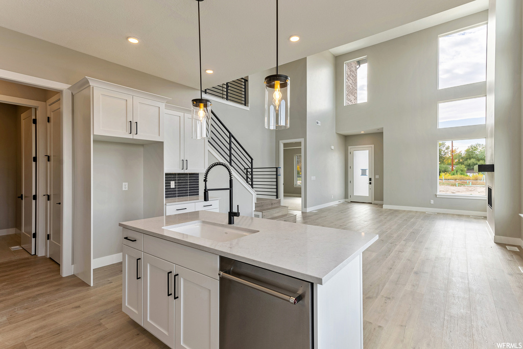 Kitchen featuring light hardwood / wood-style flooring, stainless steel dishwasher, hanging light fixtures, light stone countertops, and white cabinetry