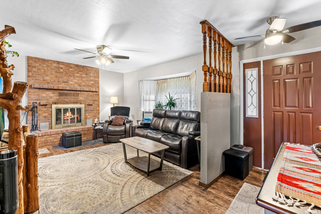 Living room featuring ceiling fan, dark wood-type flooring, a fireplace, and brick wall