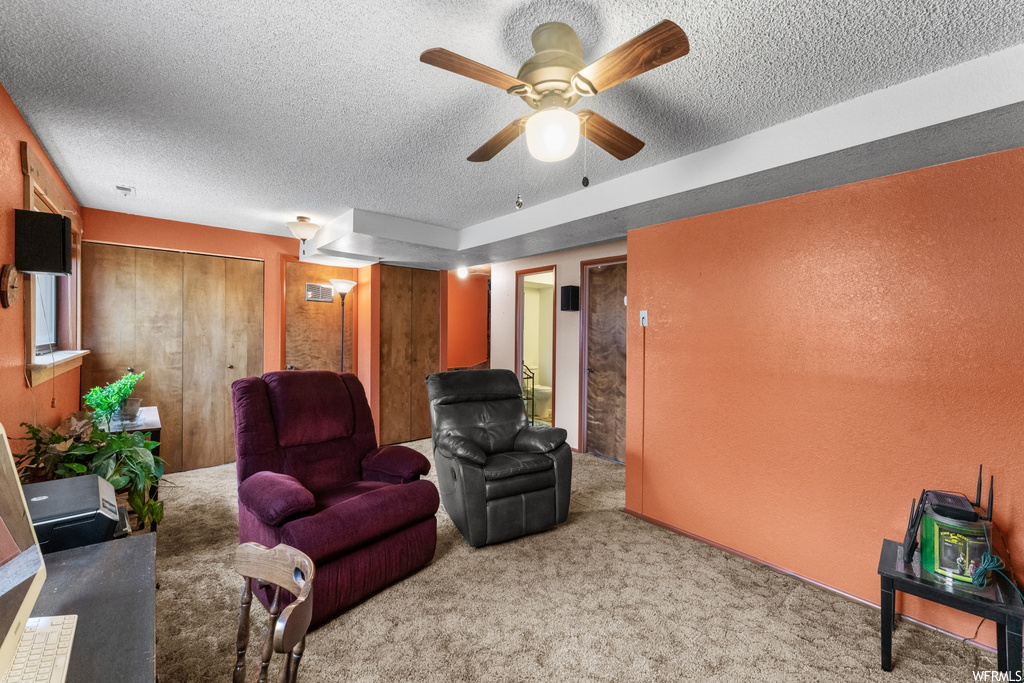 Living area with ceiling fan, a textured ceiling, and light colored carpet