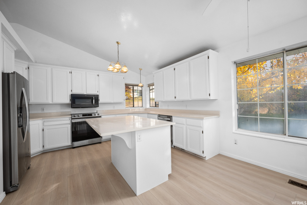 Kitchen with a kitchen island, appliances with stainless steel finishes, decorative light fixtures, and white cabinetry