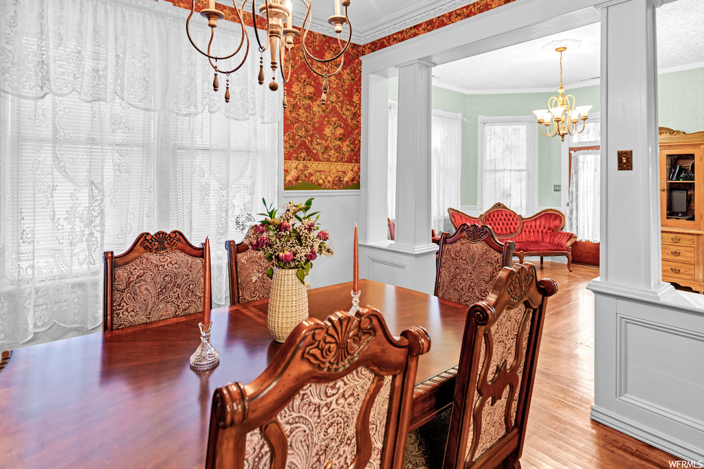 Dining space featuring ornamental molding, an inviting chandelier, decorative columns, and light hardwood / wood-style flooring