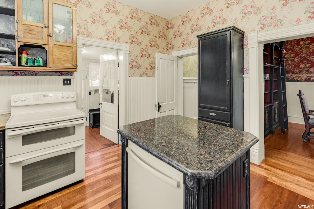 Kitchen with light hardwood / wood-style flooring, white appliances, dark stone countertops, and a kitchen island
