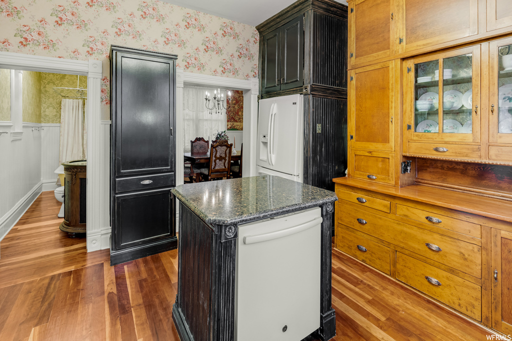 Kitchen with dark hardwood / wood-style flooring, white appliances, a chandelier, dark stone counters, and a kitchen island