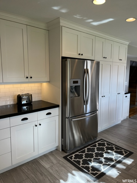 Kitchen featuring white cabinets, light wood-type flooring, tasteful backsplash, and stainless steel refrigerator with ice dispenser
