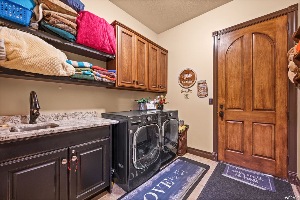 Clothes washing area featuring light tile floors, independent washer and dryer, sink, a textured ceiling, and cabinets