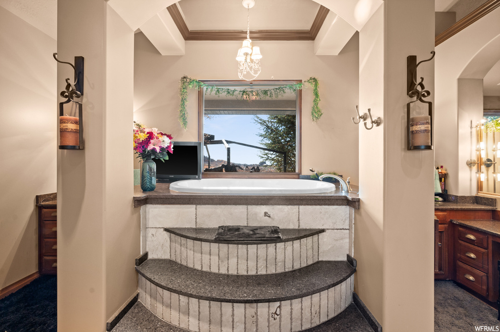 Bathroom featuring vanity, a relaxing tiled bath, an inviting chandelier, and crown molding