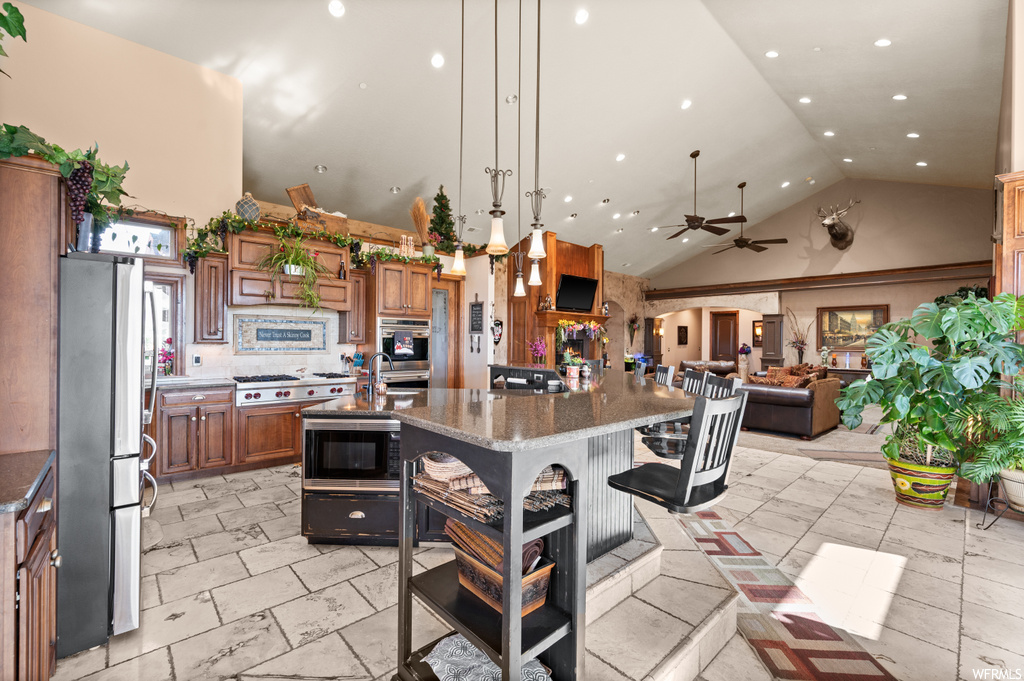 Kitchen with hanging light fixtures, stainless steel fridge, high vaulted ceiling, ceiling fan, and black microwave