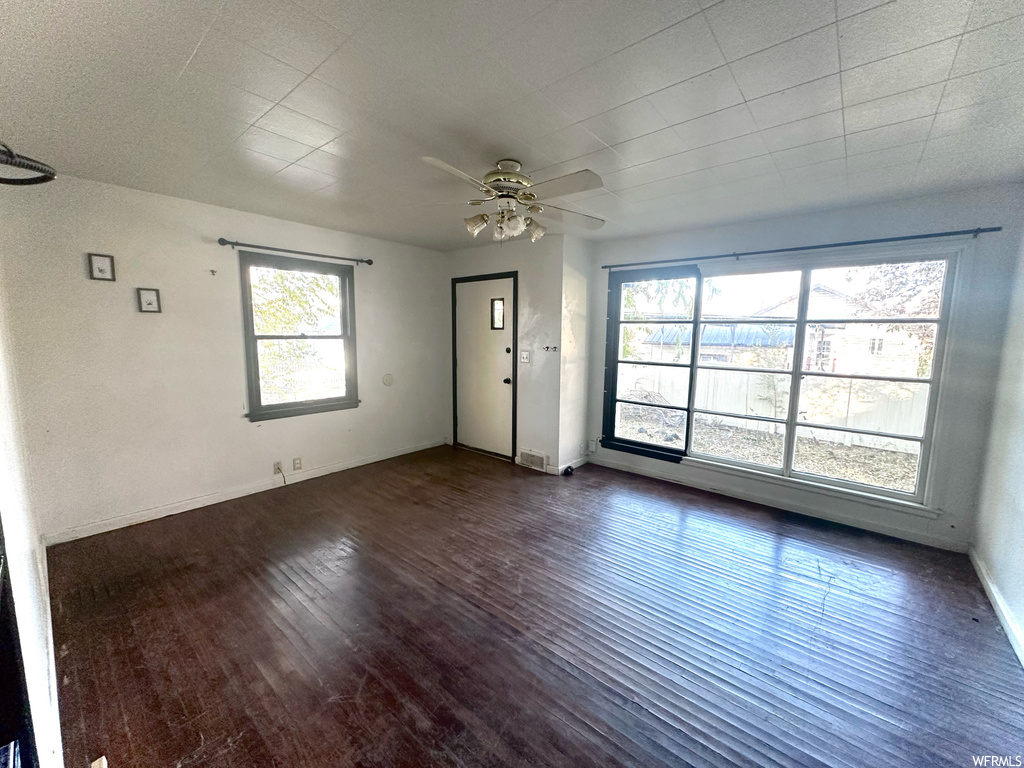 Unfurnished room featuring ceiling fan, a wealth of natural light, and dark hardwood / wood-style flooring