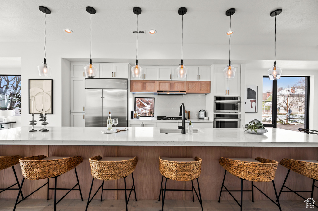 Kitchen featuring a kitchen island with sink, appliances with stainless steel finishes, and hanging light fixtures