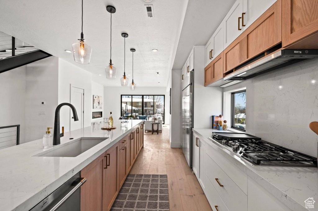 Kitchen with white cabinets, light stone countertops, light wood-type flooring, and a healthy amount of sunlight