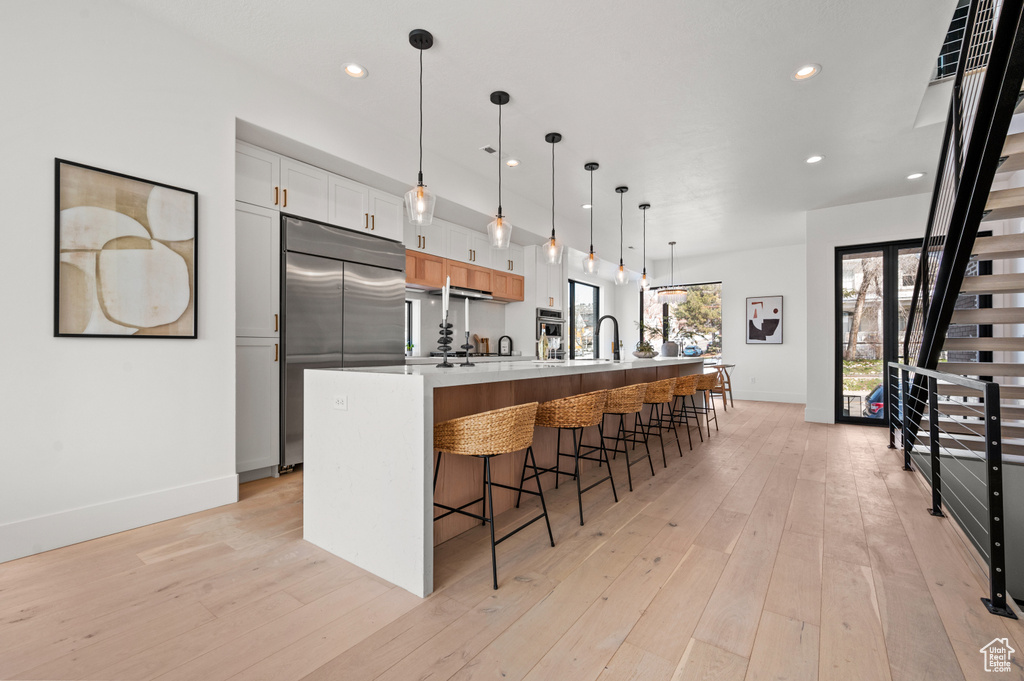 Kitchen with hanging light fixtures, light wood-type flooring, a center island with sink, white cabinetry, and stainless steel appliances