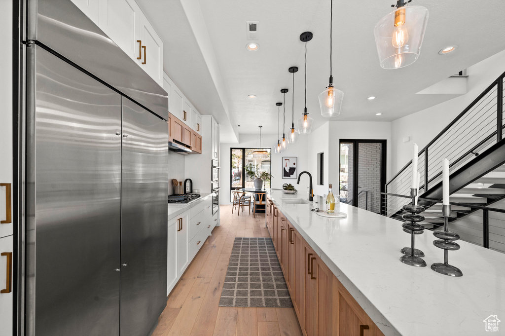 Kitchen featuring appliances with stainless steel finishes, pendant lighting, light wood-type flooring, and white cabinets