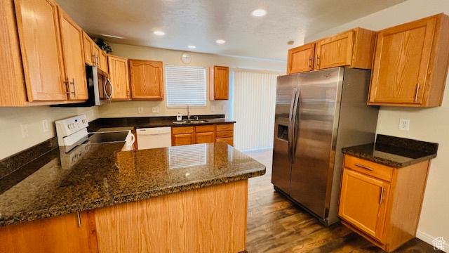 Kitchen with dark stone countertops, stainless steel appliances, dark hardwood / wood-style floors, and sink