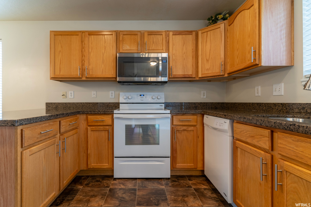 Kitchen with dark tile flooring, white appliances, and dark stone countertops