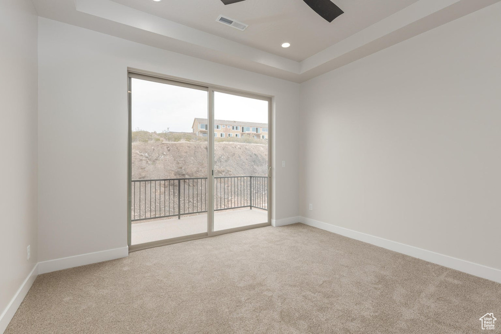 Empty room with light colored carpet, ceiling fan, and a raised ceiling