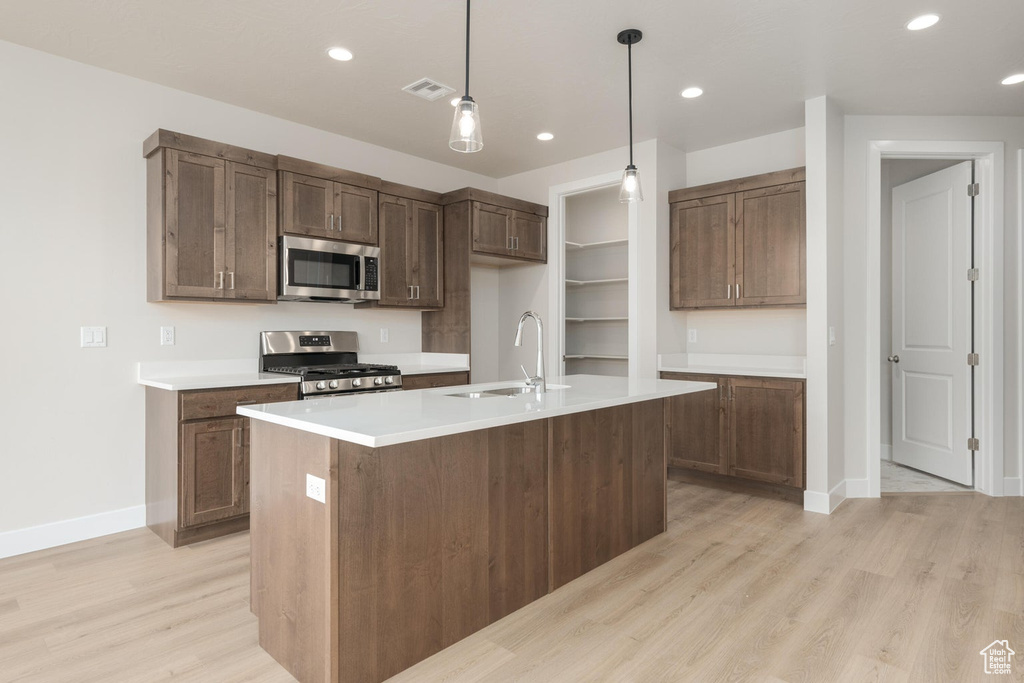 Kitchen featuring decorative light fixtures, stainless steel appliances, sink, a center island with sink, and light hardwood / wood-style flooring