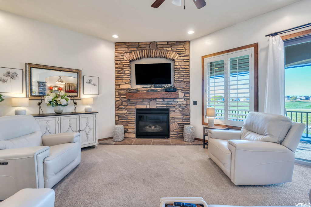 Living room featuring light carpet, ceiling fan, and a stone fireplace
