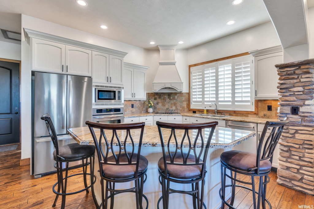 Kitchen with custom range hood, stainless steel appliances, light wood-type flooring, a kitchen island, and backsplash