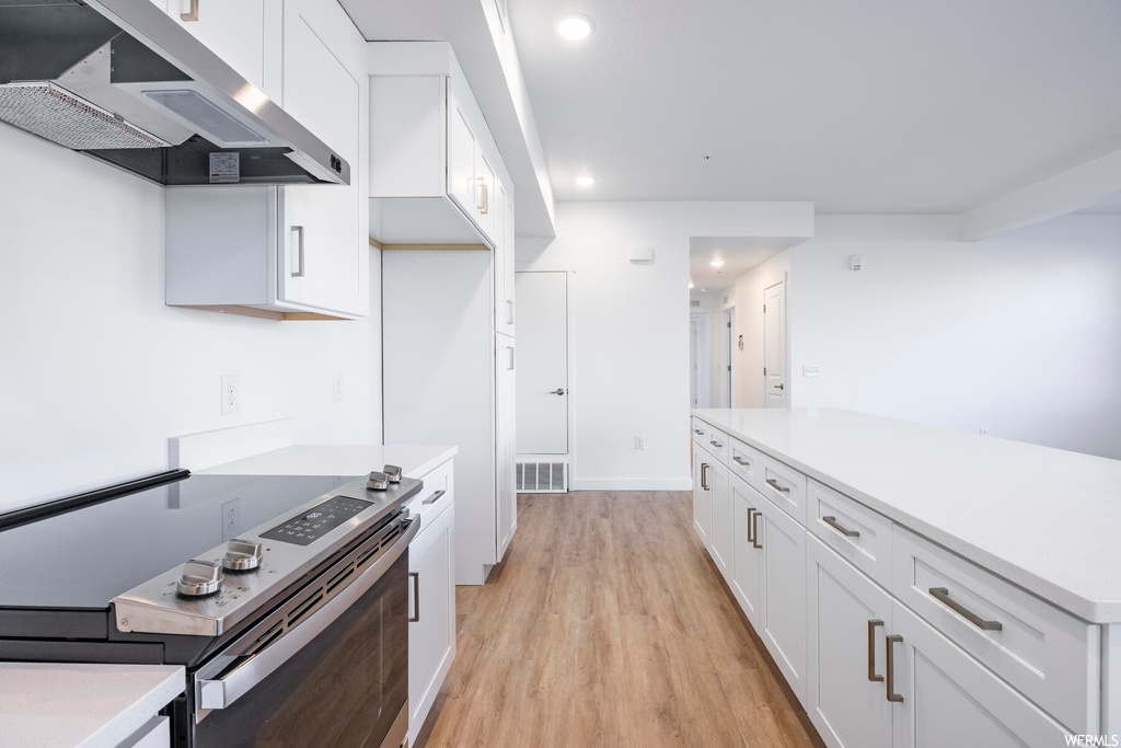 Kitchen with stainless steel range with electric cooktop, light hardwood / wood-style flooring, wall chimney range hood, and white cabinetry