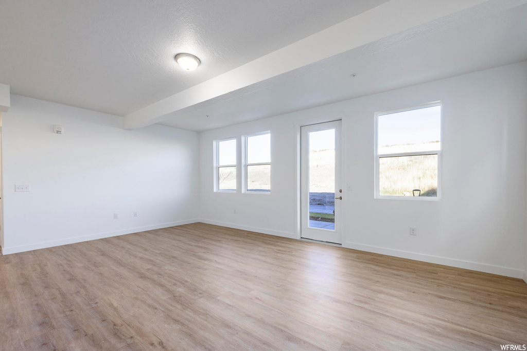 Empty room with beamed ceiling, plenty of natural light, and light hardwood / wood-style floors