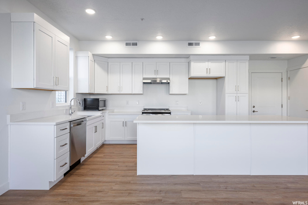 Kitchen with a center island, light wood-type flooring, stainless steel appliances, and white cabinetry