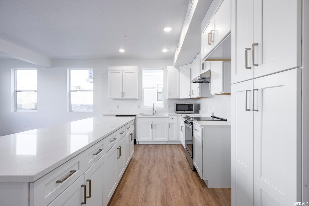 Kitchen with a center island, sink, appliances with stainless steel finishes, light wood-type flooring, and white cabinets