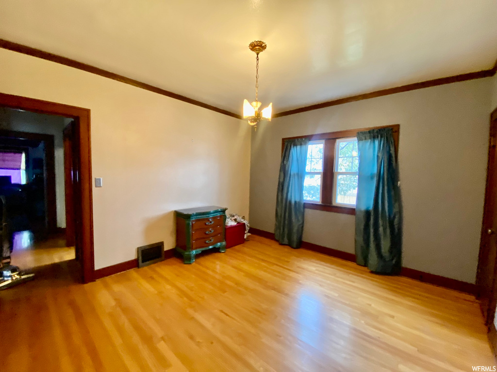 Spare room featuring a chandelier, crown molding, and light hardwood / wood-style floors