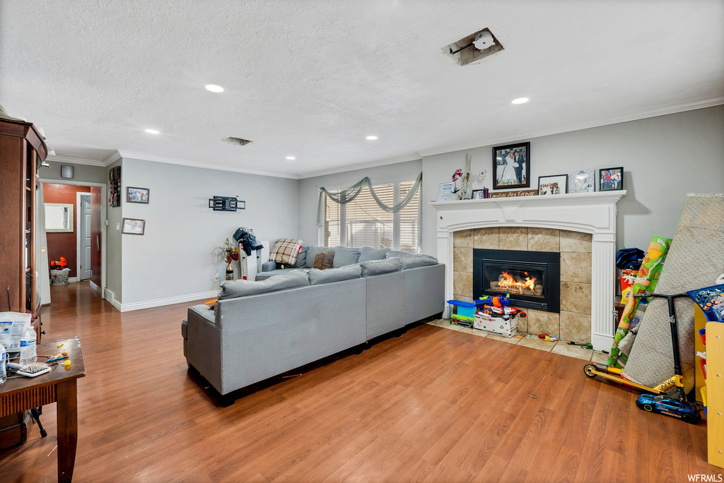 Living room featuring a tiled fireplace, a textured ceiling, hardwood / wood-style floors, and crown molding