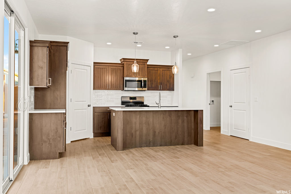 Kitchen featuring gas range, an island with sink, pendant lighting, and light hardwood / wood-style flooring