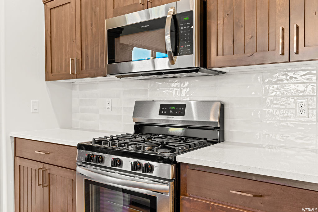 Kitchen featuring appliances with stainless steel finishes, light stone countertops, and backsplash