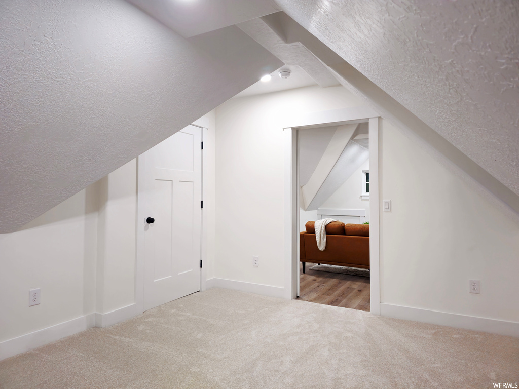 Bonus room featuring lofted ceiling, light colored carpet, and a textured ceiling