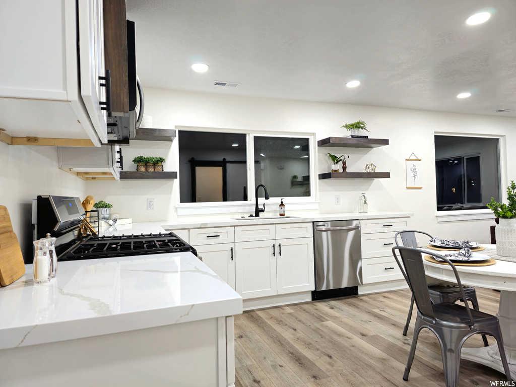 Kitchen featuring sink, light stone countertops, dishwasher, gas range oven, and white cabinetry