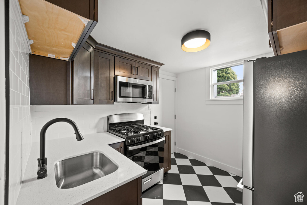 Kitchen featuring dark tile flooring, backsplash, sink, stainless steel appliances, and dark brown cabinetry