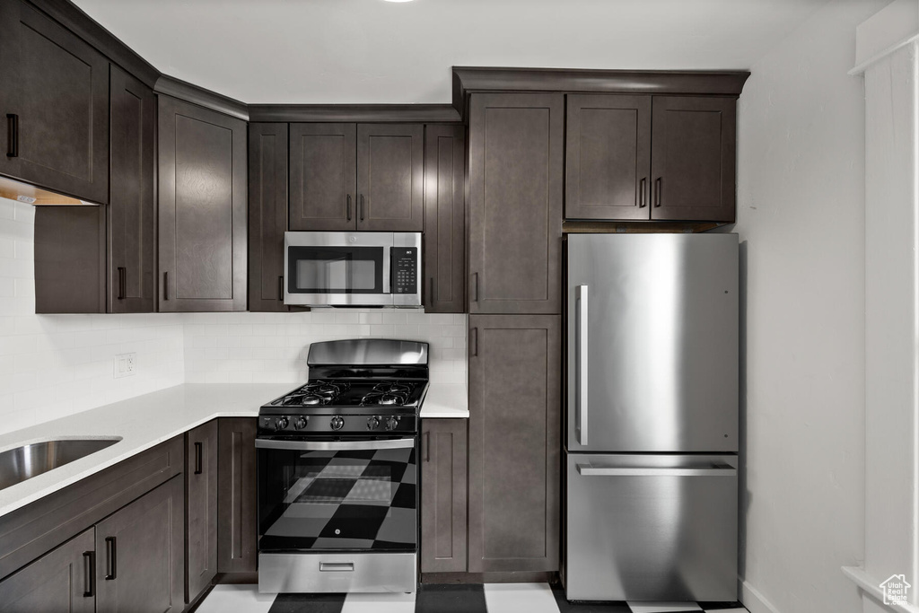 Kitchen with appliances with stainless steel finishes, dark brown cabinets, and backsplash