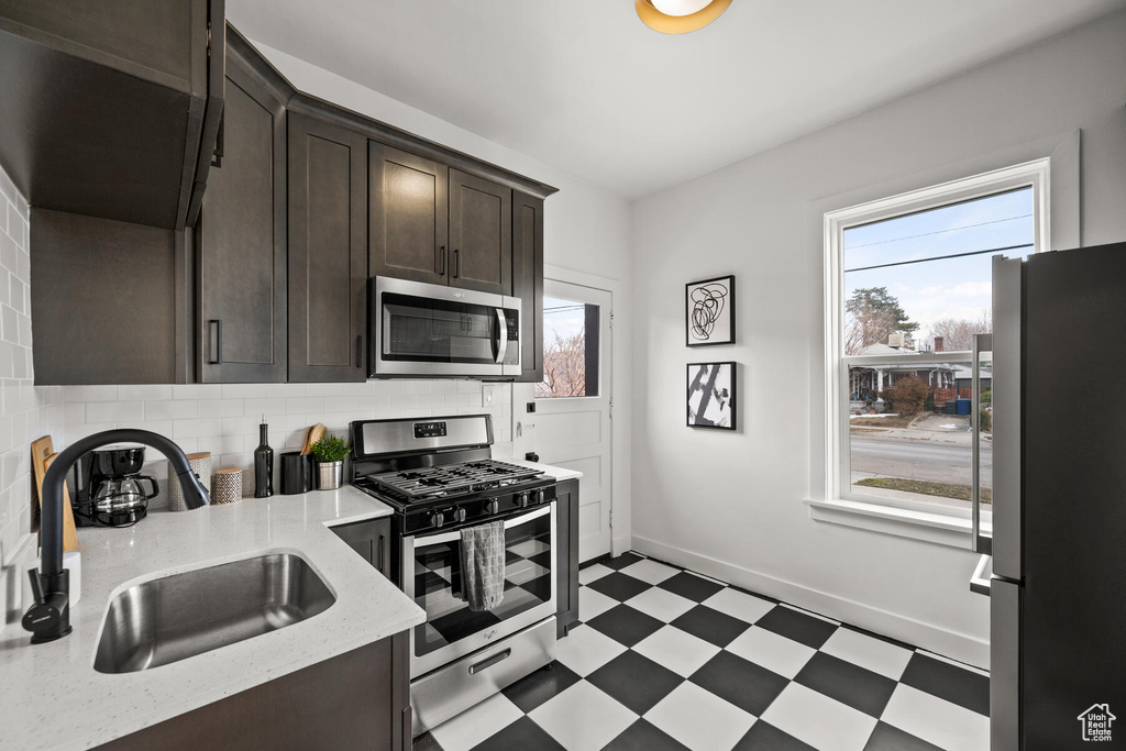 Kitchen featuring backsplash, light stone countertops, dark brown cabinets, stainless steel appliances, and light tile flooring
