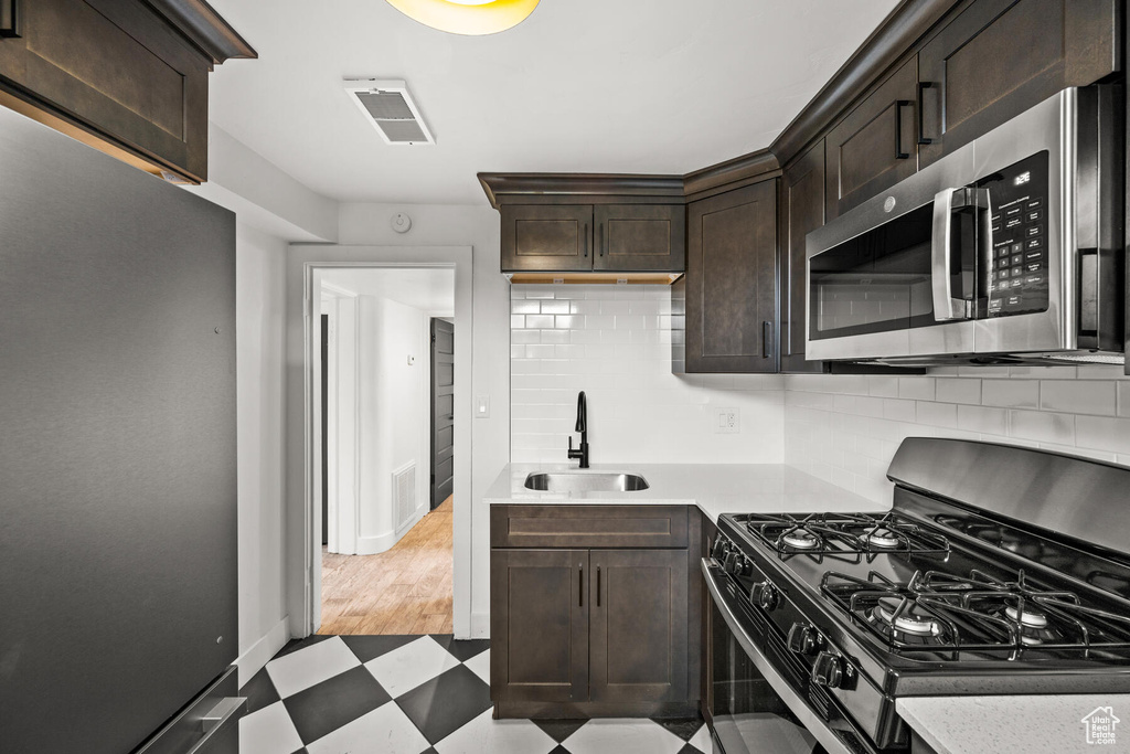 Kitchen featuring black range with gas cooktop, light tile floors, dark brown cabinetry, and sink