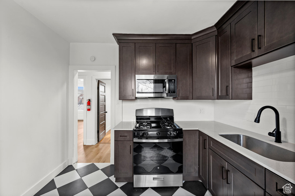 Kitchen with stainless steel appliances, tasteful backsplash, dark brown cabinetry, sink, and light tile floors