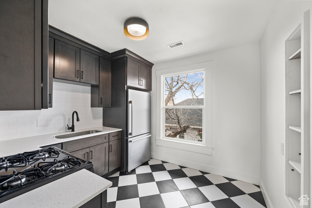 Kitchen featuring stainless steel refrigerator, backsplash, dark brown cabinets, sink, and light tile floors