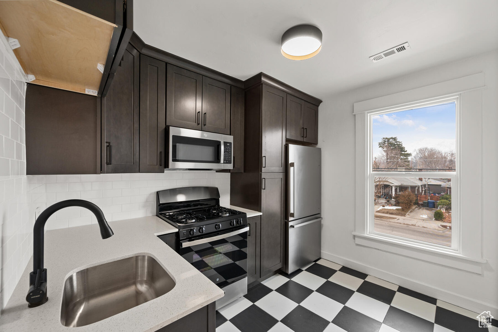 Kitchen with stainless steel appliances, dark brown cabinetry, tasteful backsplash, sink, and light tile floors