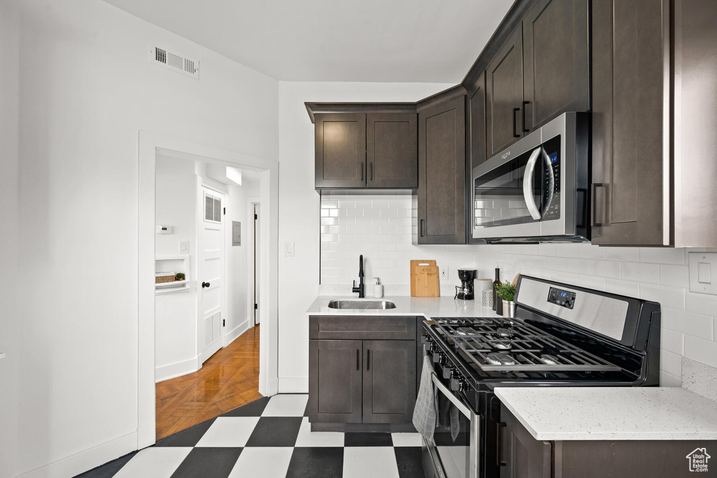 Kitchen featuring backsplash, dark parquet floors, sink, stainless steel appliances, and dark brown cabinetry